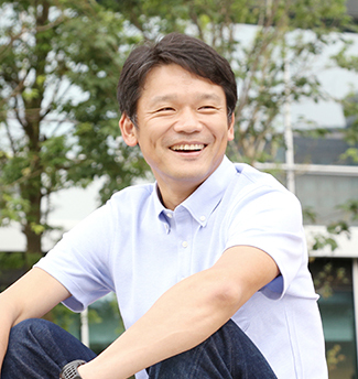 木々を背景に笑顔の宮坂学