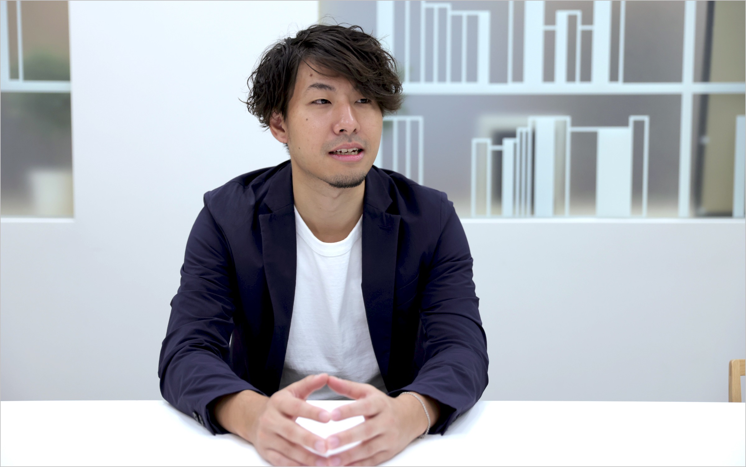 菅原が椅子に座りながら、自身の担当業務についてインタビューに答えている様子の写真