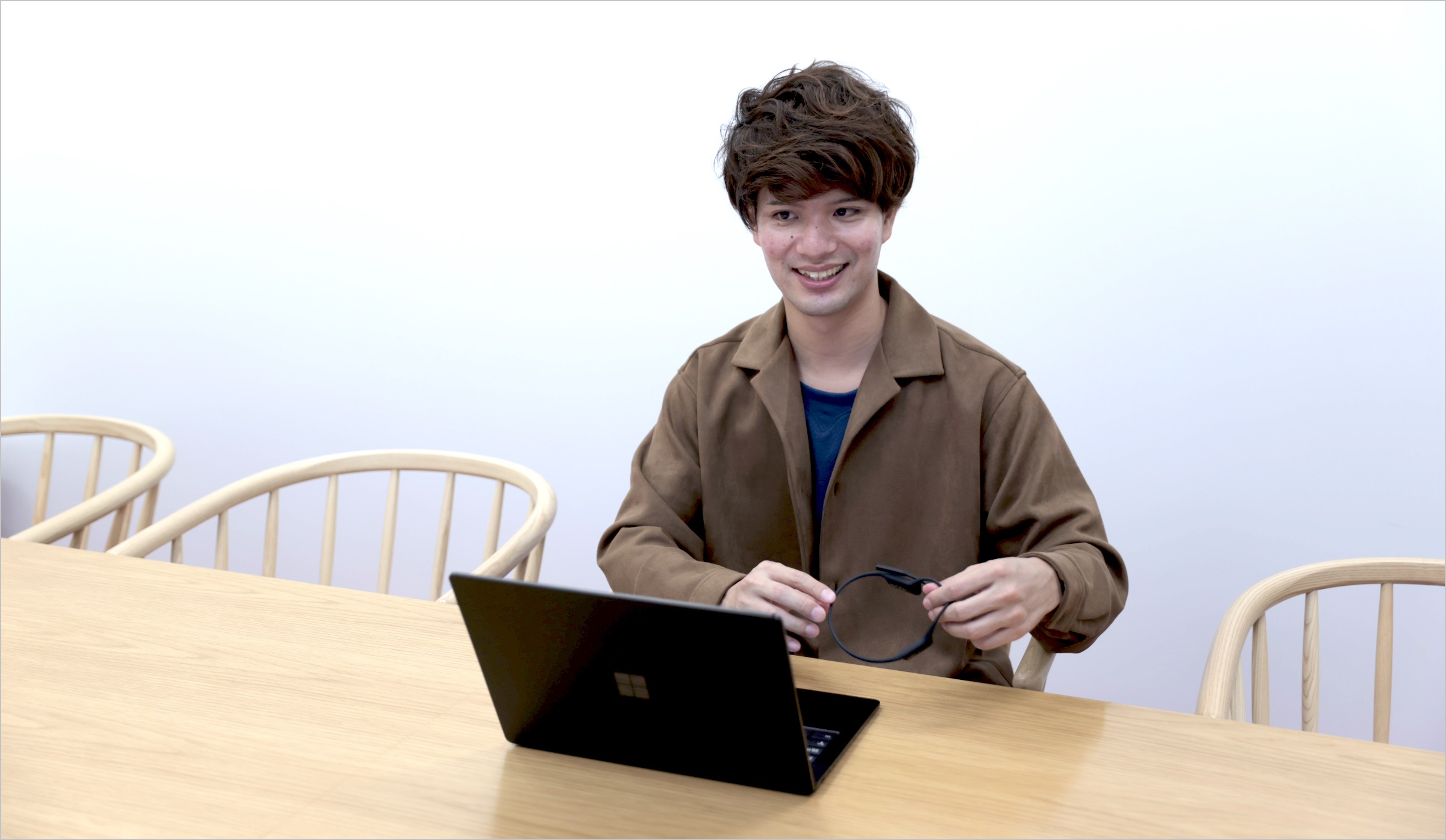 小林が椅子に座りパソコンの前で笑顔でインタビューに答えている様子の写真