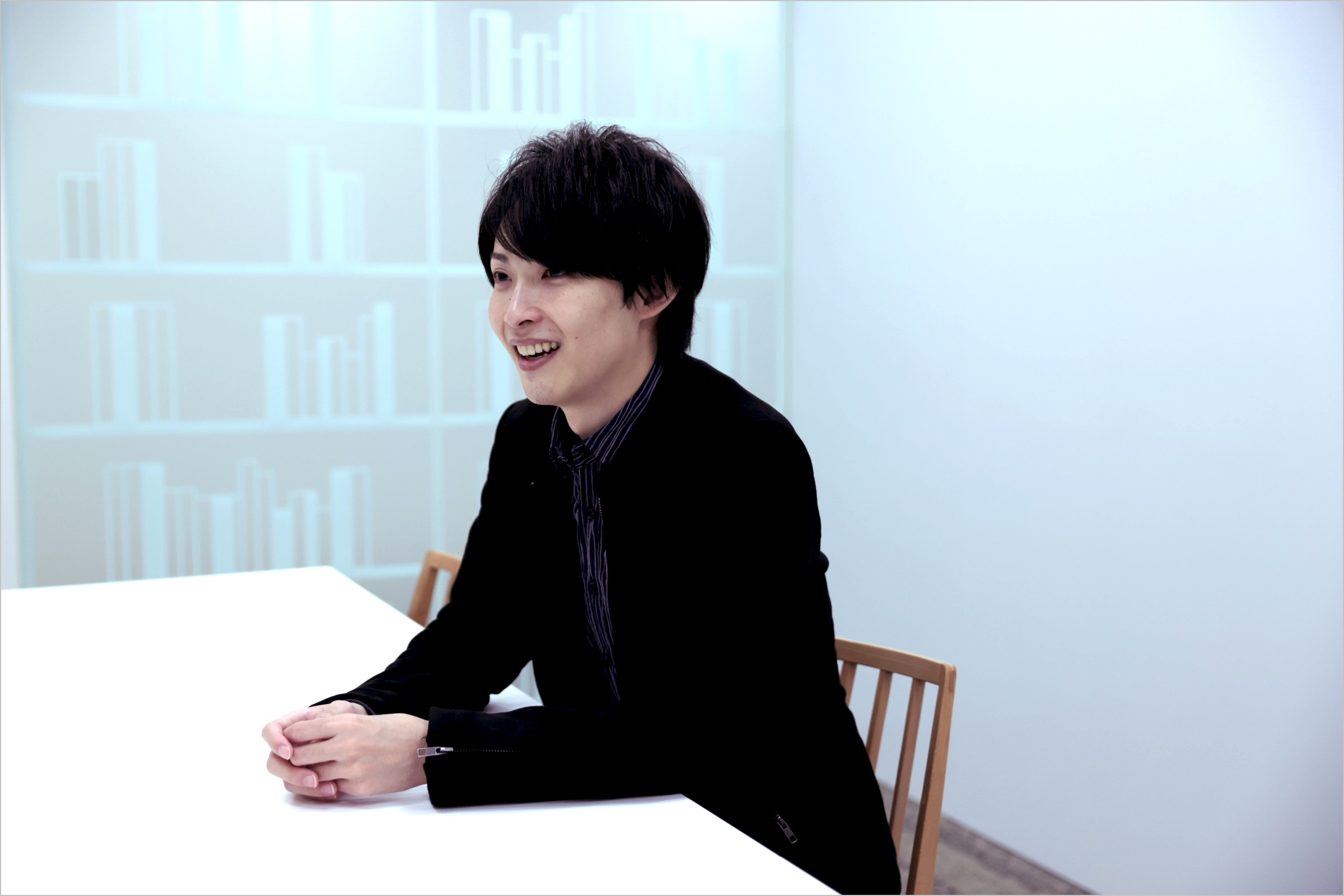 坂本が椅子に座り笑顔でインタビューに答えている様子の写真