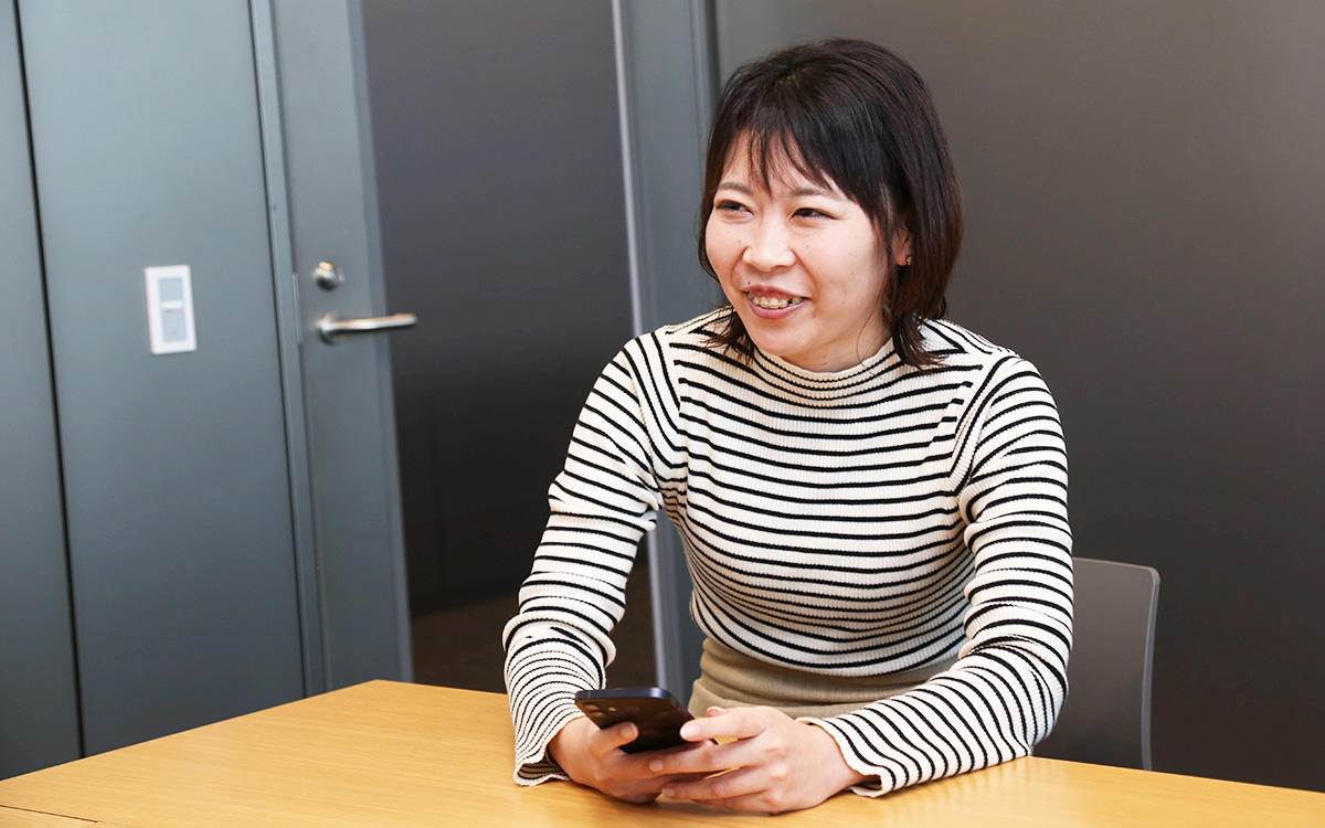 スマホを持つストライプの服を着た女性が笑顔で座っています。