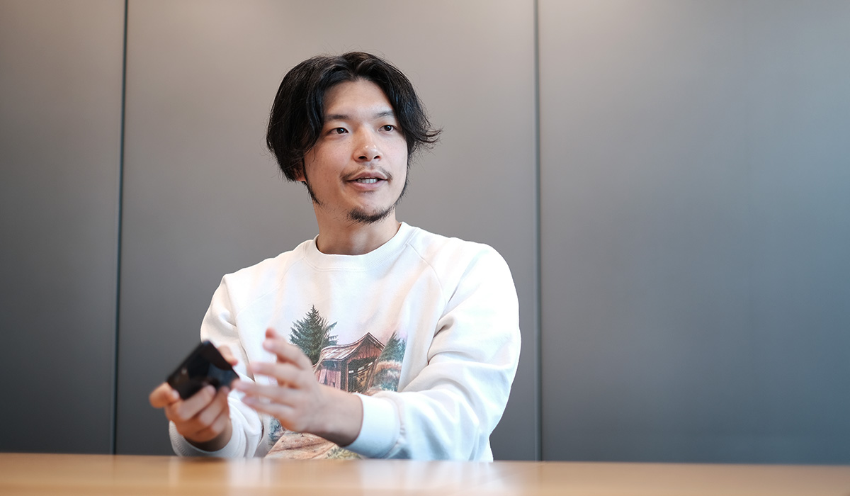 白い服の男性が手に何かを持って話しています。