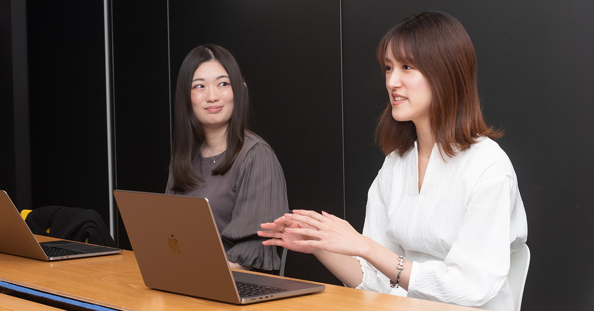 二人の女性がノートパソコンを前に話している場面。