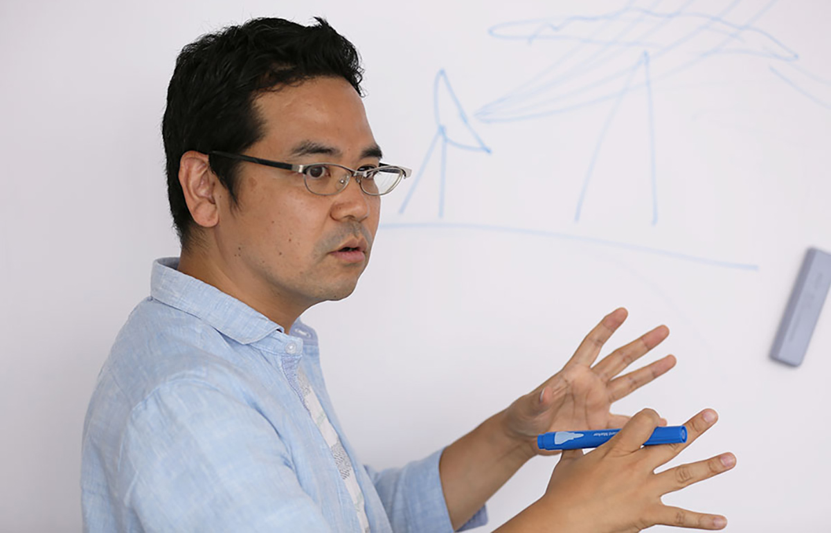 メガネをかけた男性がホワイトボードに図を描きながら説明している。