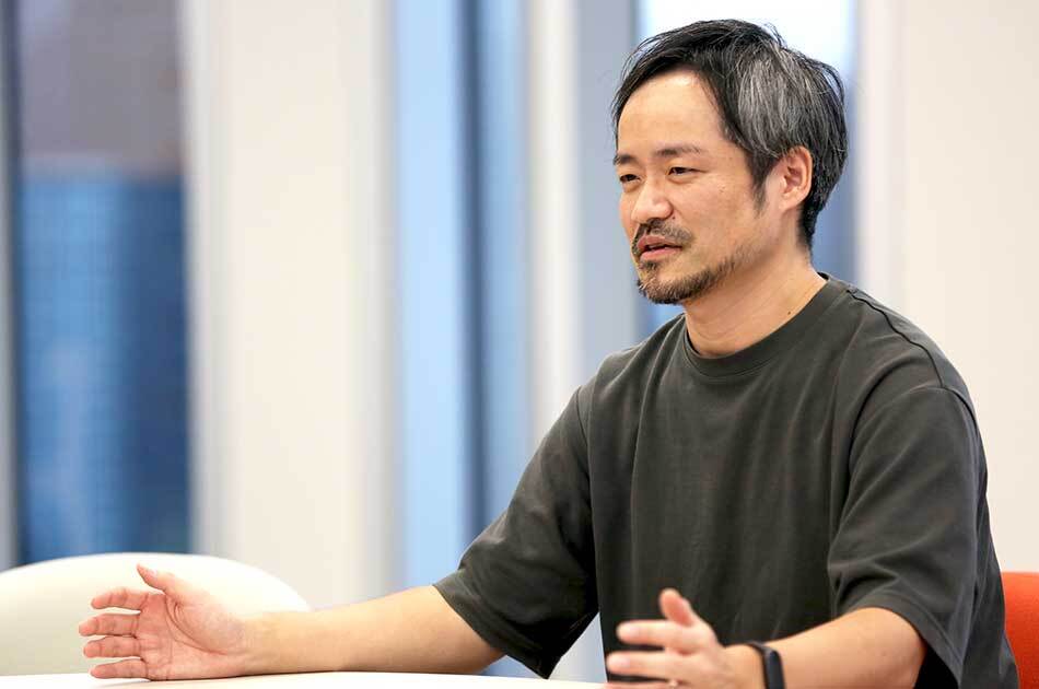 男性がインタビュー中の様子。背景には窓があり、手を広げて話している。