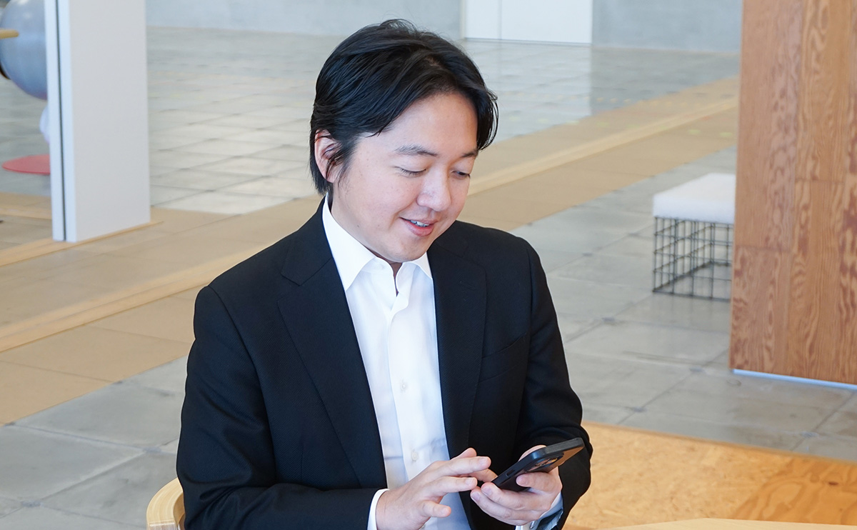 スーツ姿の男性がスマートフォンを見ながら微笑んでいる。