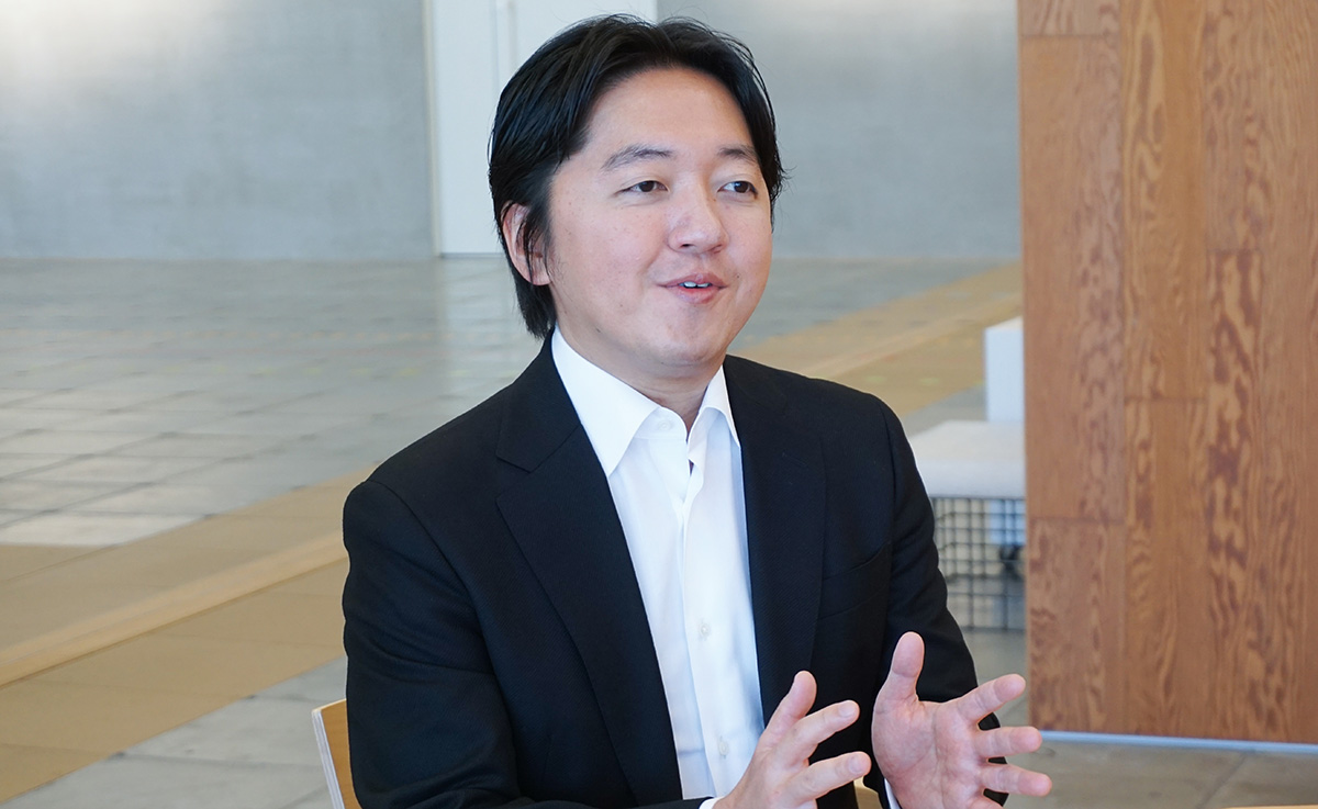 スーツ姿の男性が手を広げて話している。