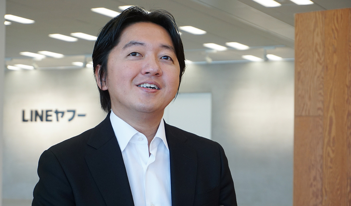 スーツ姿の男性が笑顔で話している。背景に「LINEヤフー」のロゴ。