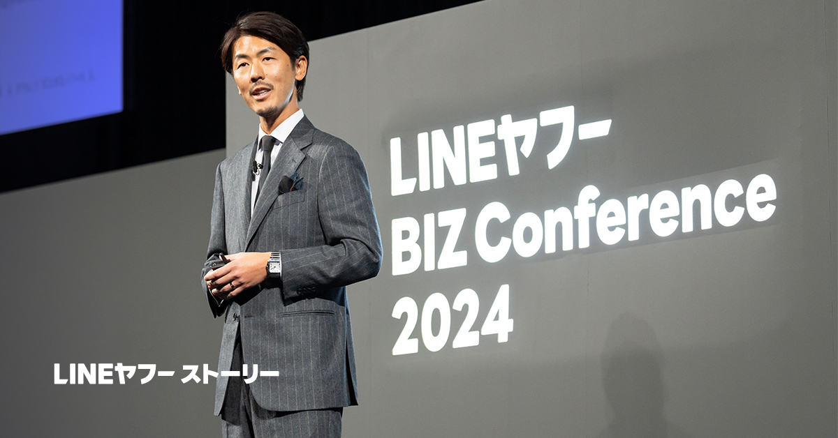スーツを着た男性が「LINEヤフーBIZ Conference 2024」でプレゼンテーションを行っている様子です。