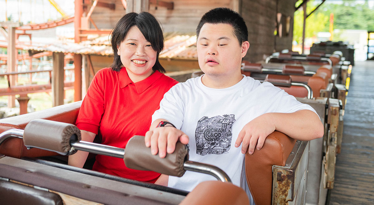 ジェットコースターの座席に座る女性と少年。二人とも笑顔で、これからの乗車を楽しみにしている。