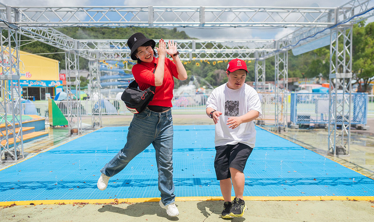 女性と男の子が屋外で楽しそうにジャンプしている。背景には遊具が見える。