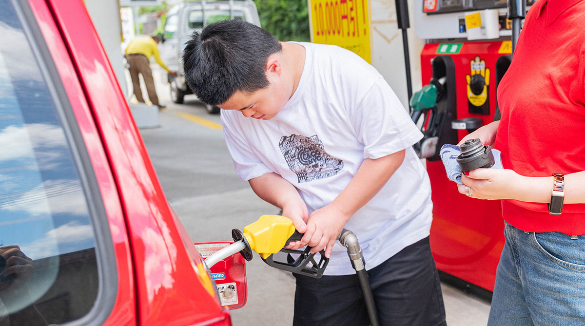 男の子がガソリンスタンドで赤い車に給油している様子。