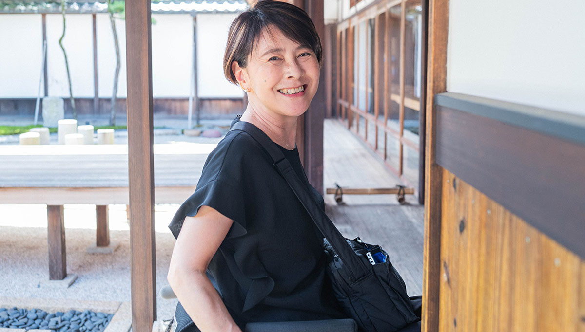 伝統的な建物の縁側で笑顔を見せる女性。