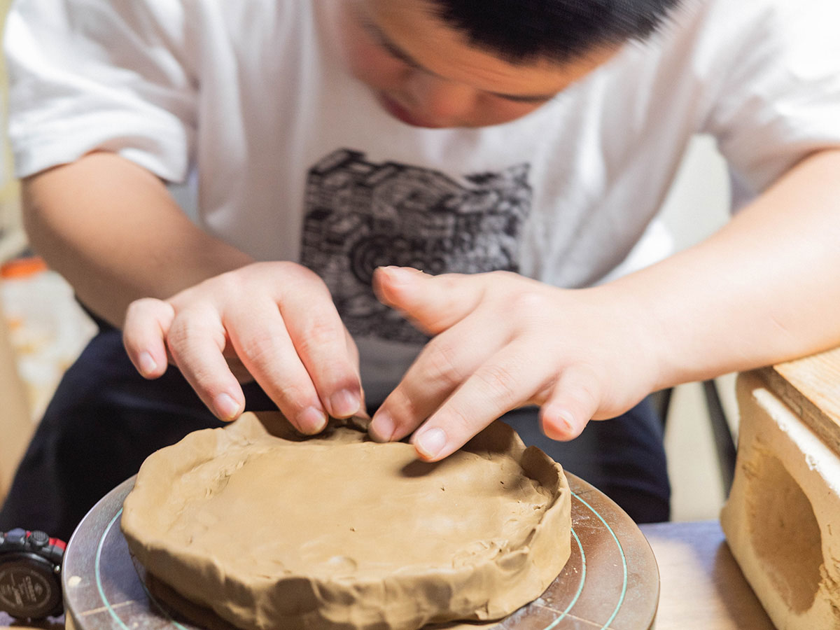 子供が粘土を使って作品を作成中。真剣な表情で手を動かし、形を整えている。