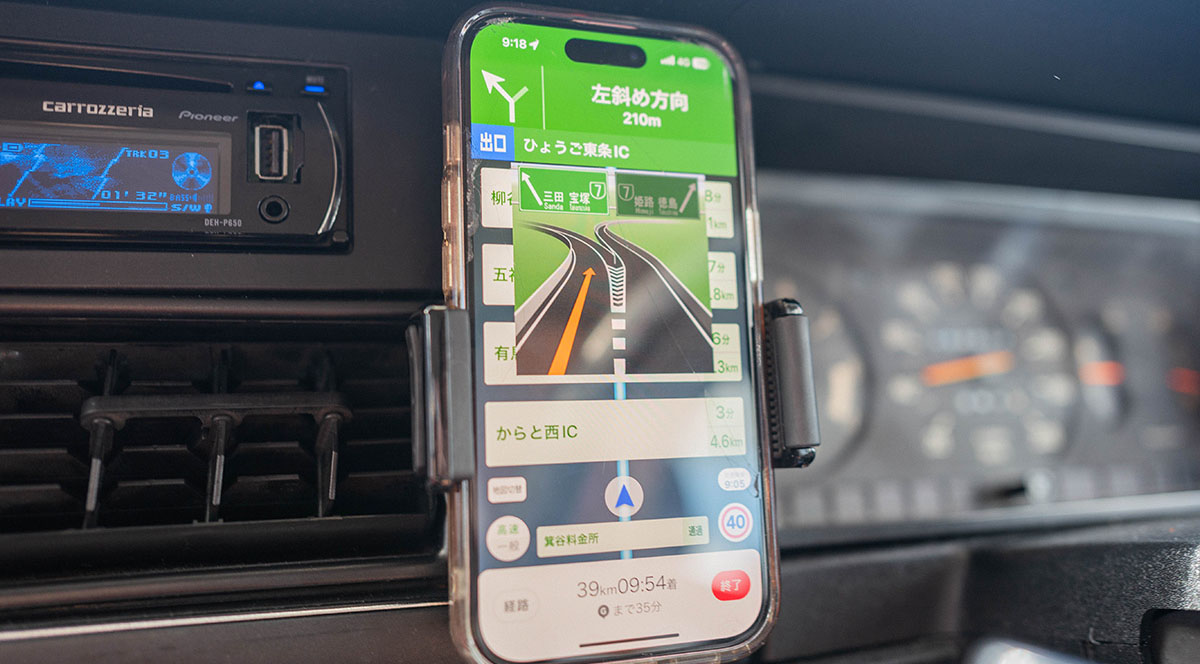 車内のスマートフォンがナビゲーションアプリを表示し、次の出口までの距離を案内している。