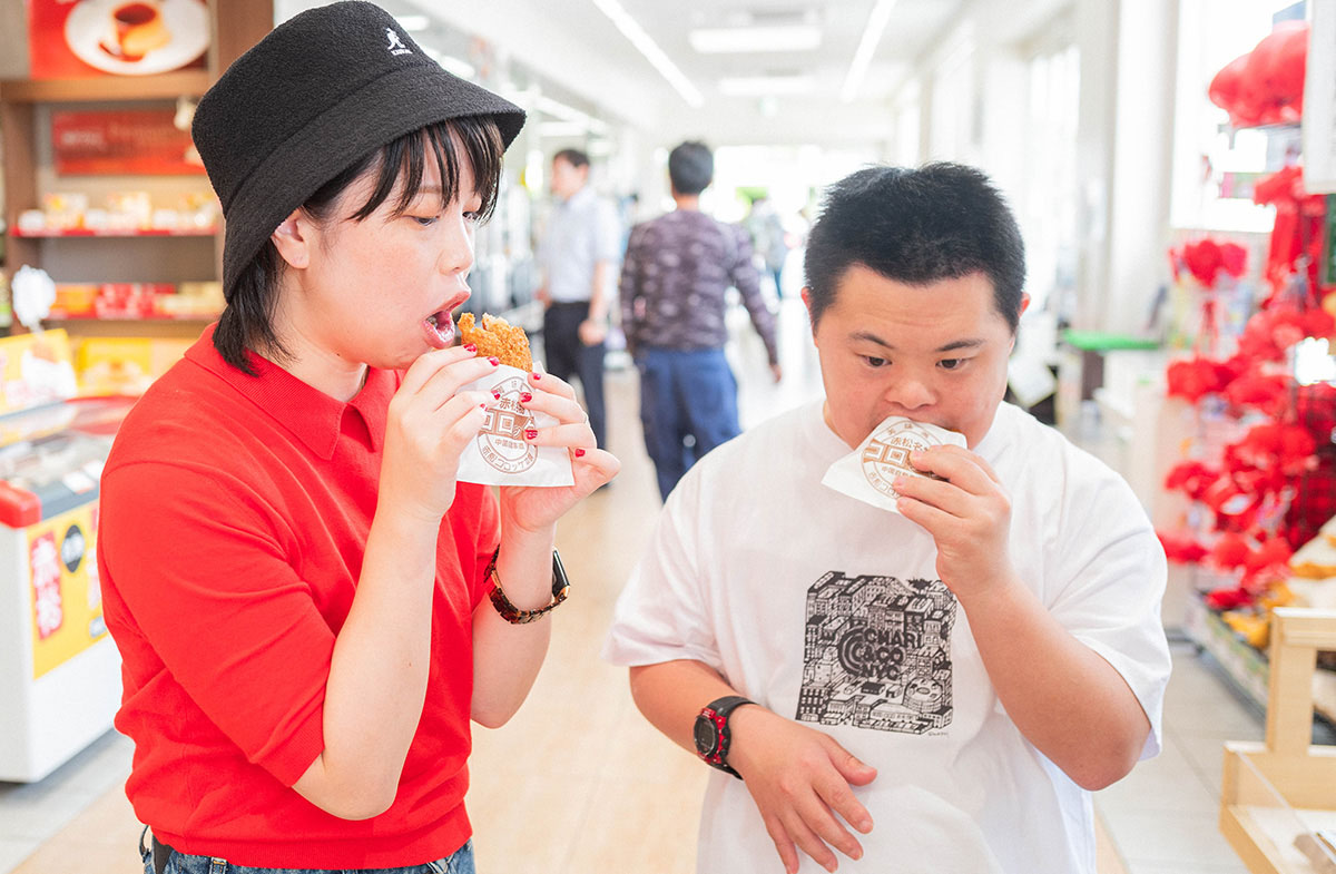 店内で女性と少年が軽食を楽しんでいる。明るい雰囲気の中で、二人は食べ物を味わう。