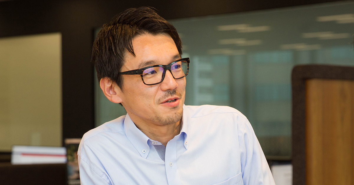 男性がインタビュー中の様子。眼鏡をかけ、リラックスした雰囲気で話している。