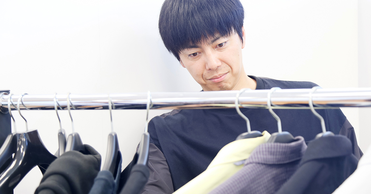 男性が服のラックを見ながら、考え込んでいる様子。様々な色の服がかかっている。