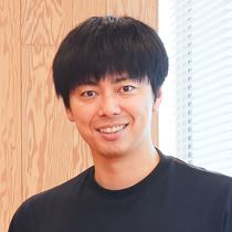 黒いシャツを着た男性がカメラに向かって笑顔を見せている。明るい室内で撮影。西村さんのアイコン。