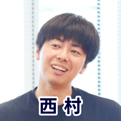 黒いシャツを着た男性がカメラに向かって笑顔を見せている。明るい室内で撮影。西村さんのアイコン。