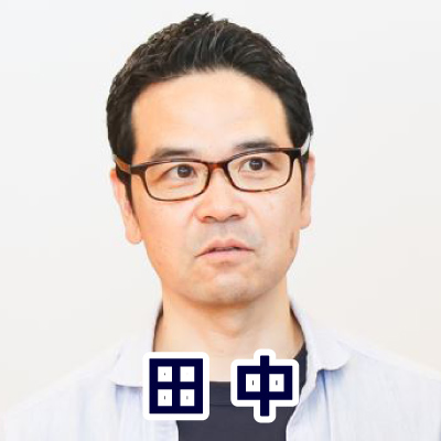 眼鏡をかけた男性が正面を向いて話している。カジュアルな服装で、落ち着いた雰囲気。田中さんのアイコン。