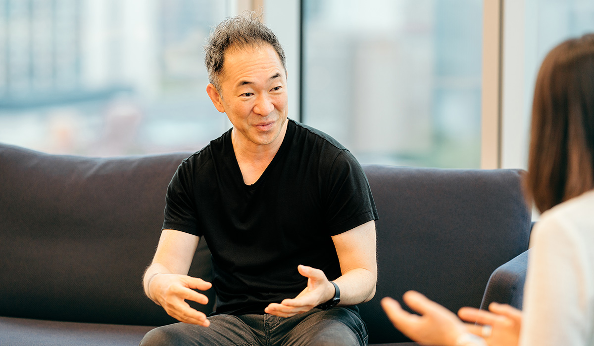男性がソファに座り、手を使って話をしている。対面の人物と活発に会話をしている様子。