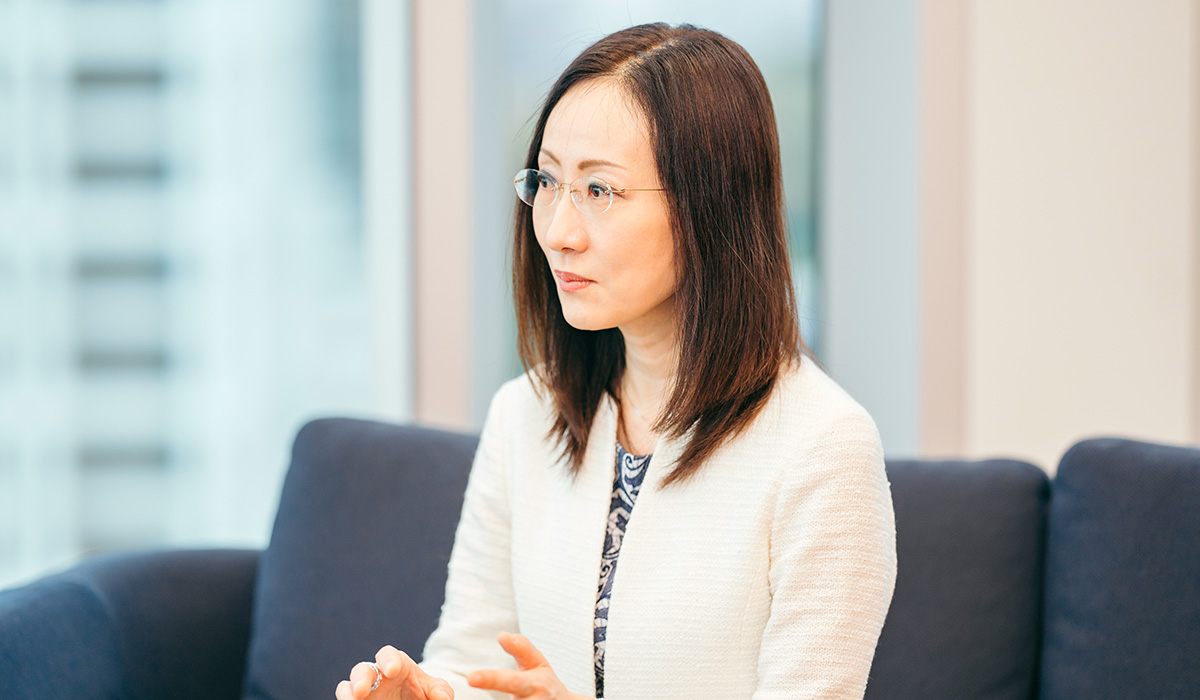 女性がソファに座り、真剣な表情で話を聞いている。背景には窓があり、都会の景色が見える。