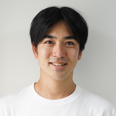 白いシャツを着た男性が微笑んでいる。背景はシンプルな白色。