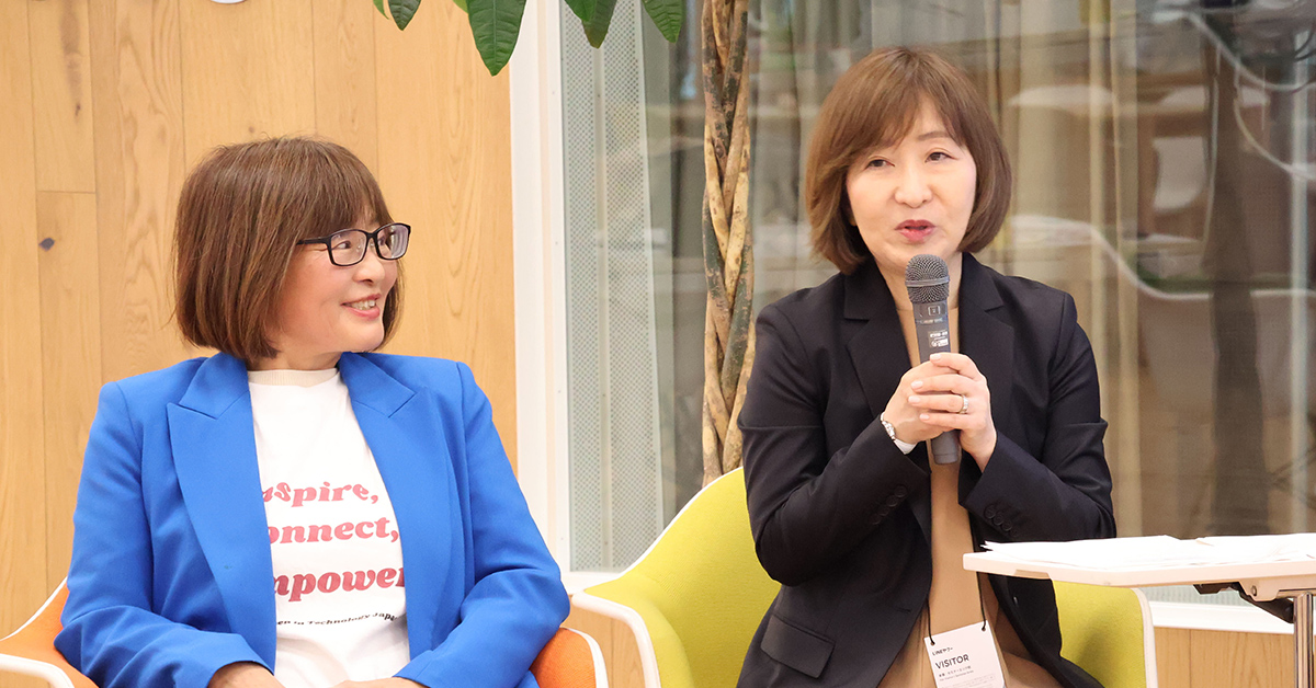 2人の女性が座って会話中。1人は青いジャケット、もう1人は黒いジャケットを着ています。