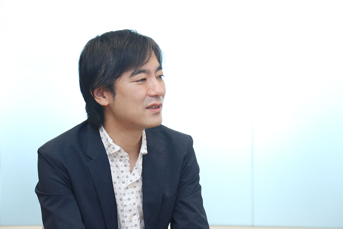 スーツを着た男性が、もう一人の男性と会話をしています。笑顔でリラックスした雰囲気です。