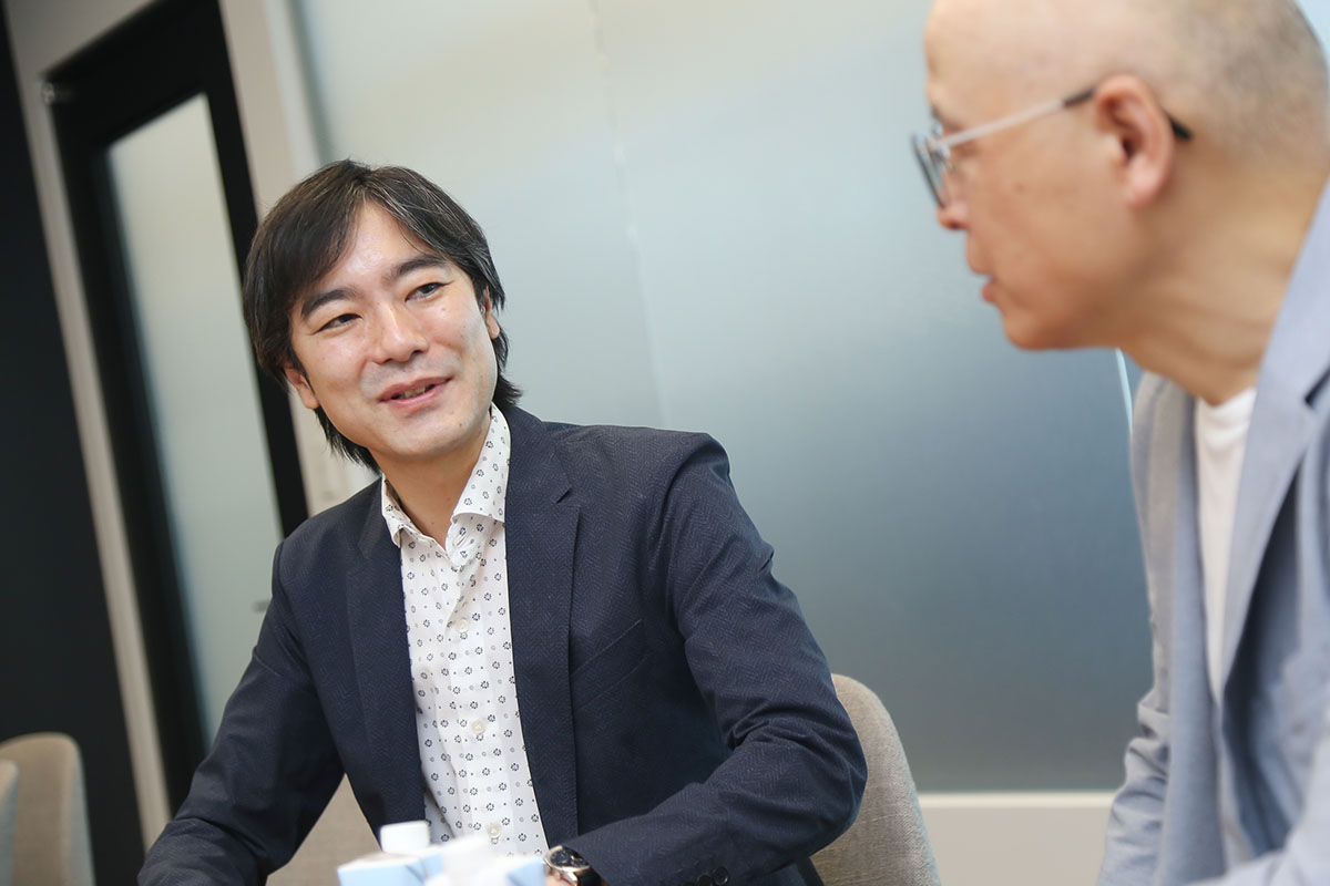 スーツを着た男性が、もう一人の男性と笑顔で話をしています。親しみやすい雰囲気です。