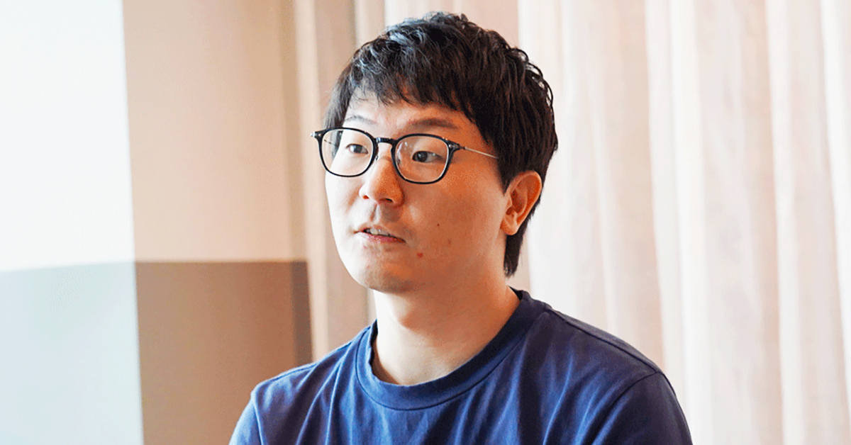 眼鏡をかけた男性がカジュアルな服装で話しています。