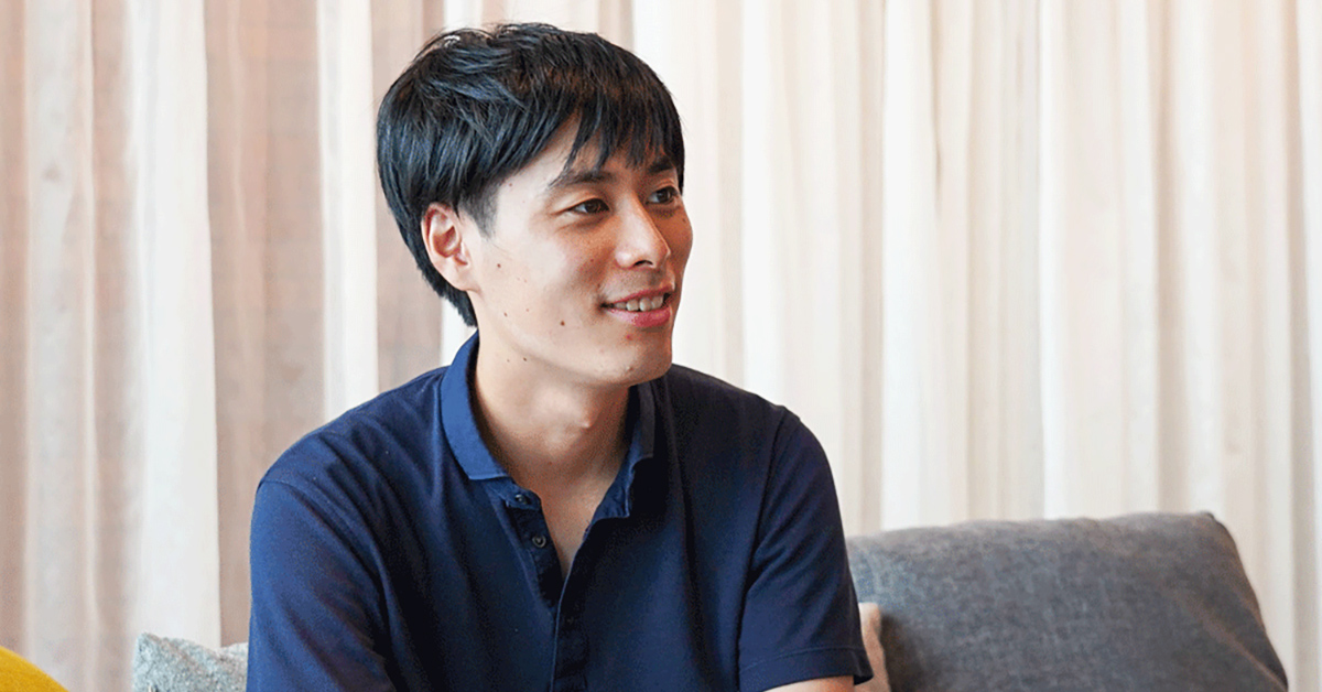 カジュアルな服装の男性が微笑んで座っています。
