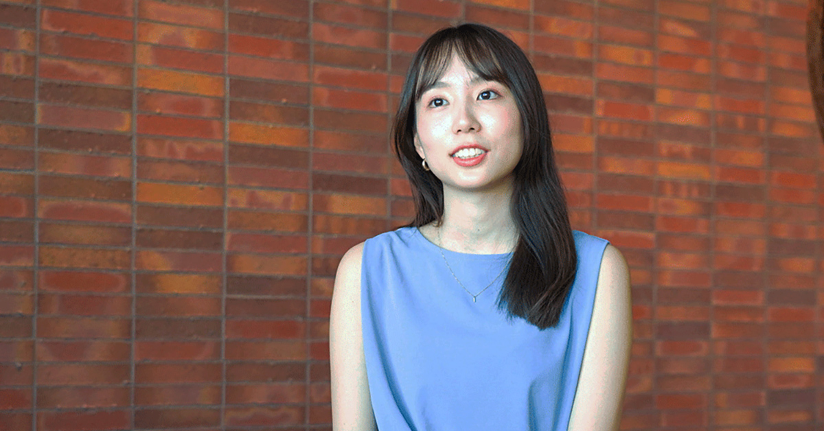 青い服の女性がレンガの壁の前で微笑んでいます。