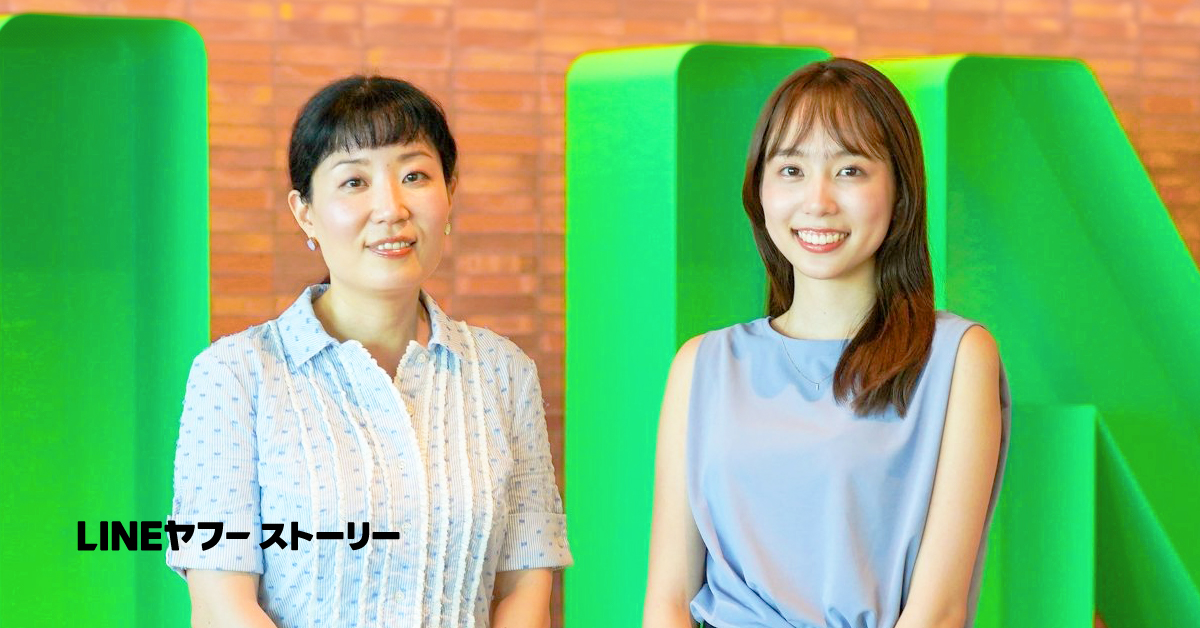 青い服の女性がレンガの壁の前で微笑んでいます。