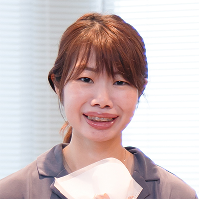 女性が室内で微笑んでいる。背景のブラインドが光を通し、明るい雰囲気が漂う。