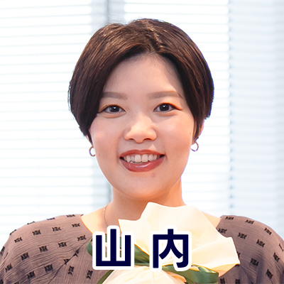 女性が室内で微笑み、背景のブラインドが光を通している。名前が「山内」と表示されている。