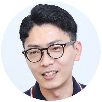 眼鏡をかけた男性が笑顔で話している。背景は白く、カジュアルな服装をしている。