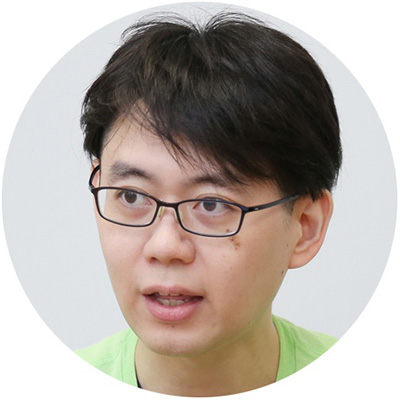 眼鏡をかけた男性が真剣な表情で何かを見ている。背景は白く、カジュアルな服装。