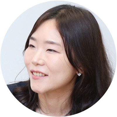 女性が笑顔で話している。背景は白く、黒い服を着ている。