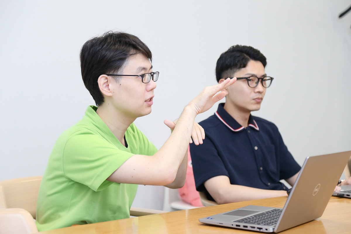 二人の男性がノートパソコンを前にして話し合っている。真剣な様子。