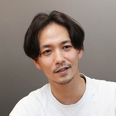 白いシャツを着た男性が微笑んでいる。リラックスした表情で、カジュアルな雰囲気が漂う。