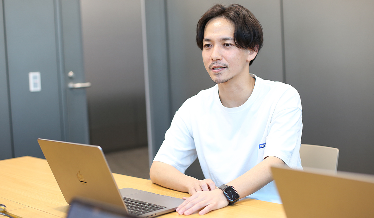 白いシャツの男性が会議室でノートパソコンを使っている。真剣な表情で話をしている。