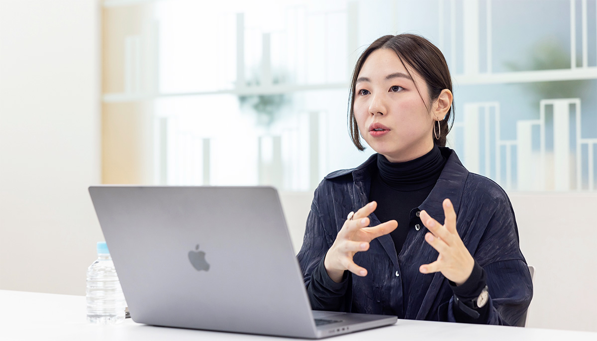女性がノートパソコンを前に話している様子。テーブルには水のボトルが置かれている。