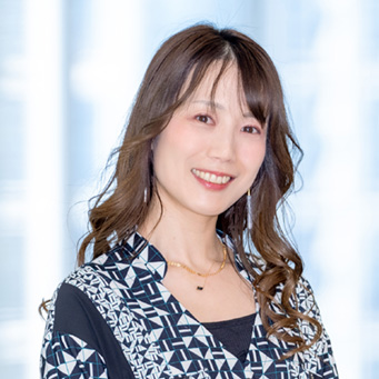 笑顔の女性が幾何学模様の服を着て正面を向いている。