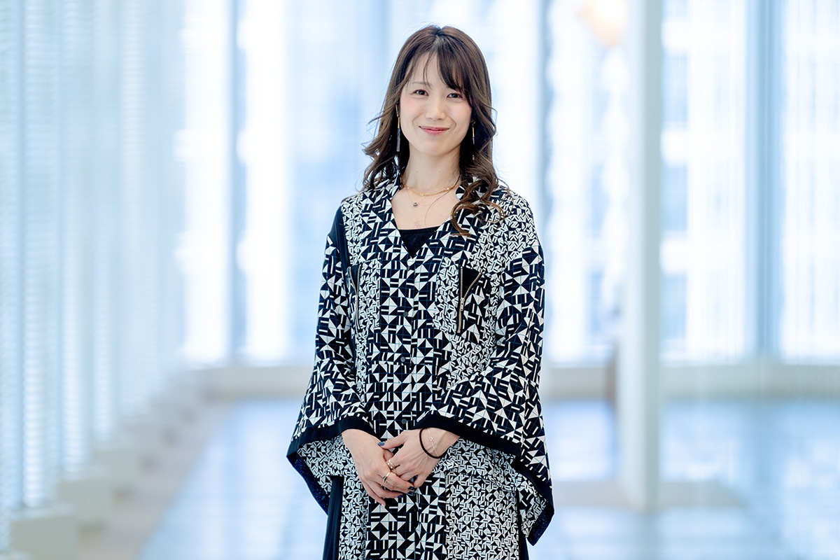 幾何学模様の服を着た女性が明るい廊下で微笑んでいる。
