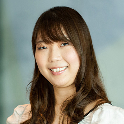 長い髪の女性が微笑んでいる。背景はぼやけた室内。