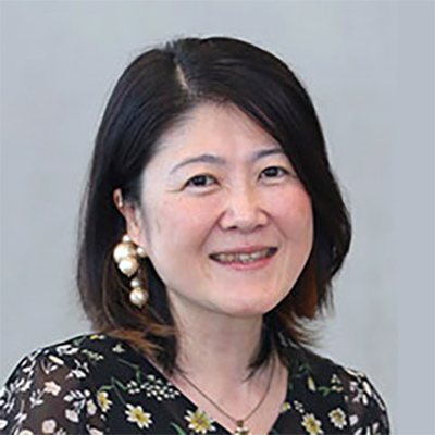 短い髪の女性が微笑んでいる。背景はグレー。