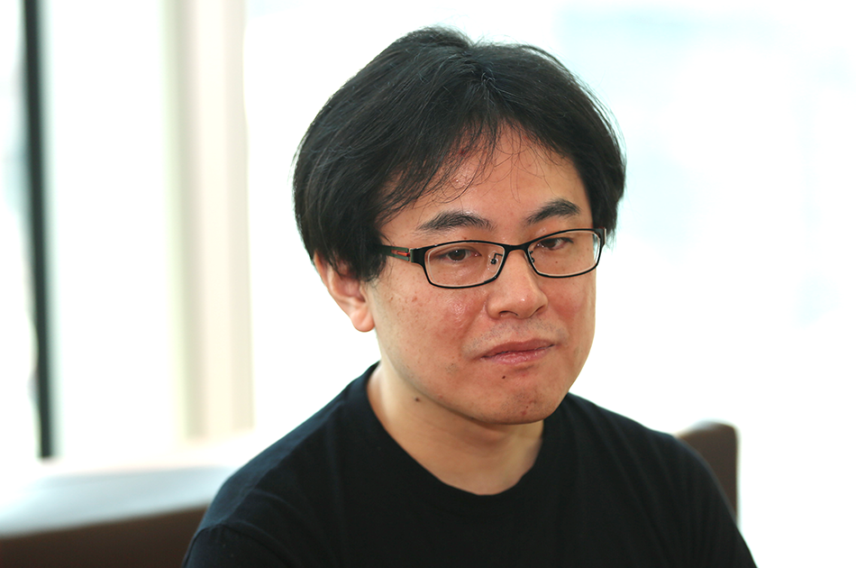 メガネをかけた男性が、室内で真剣な表情をしている。
