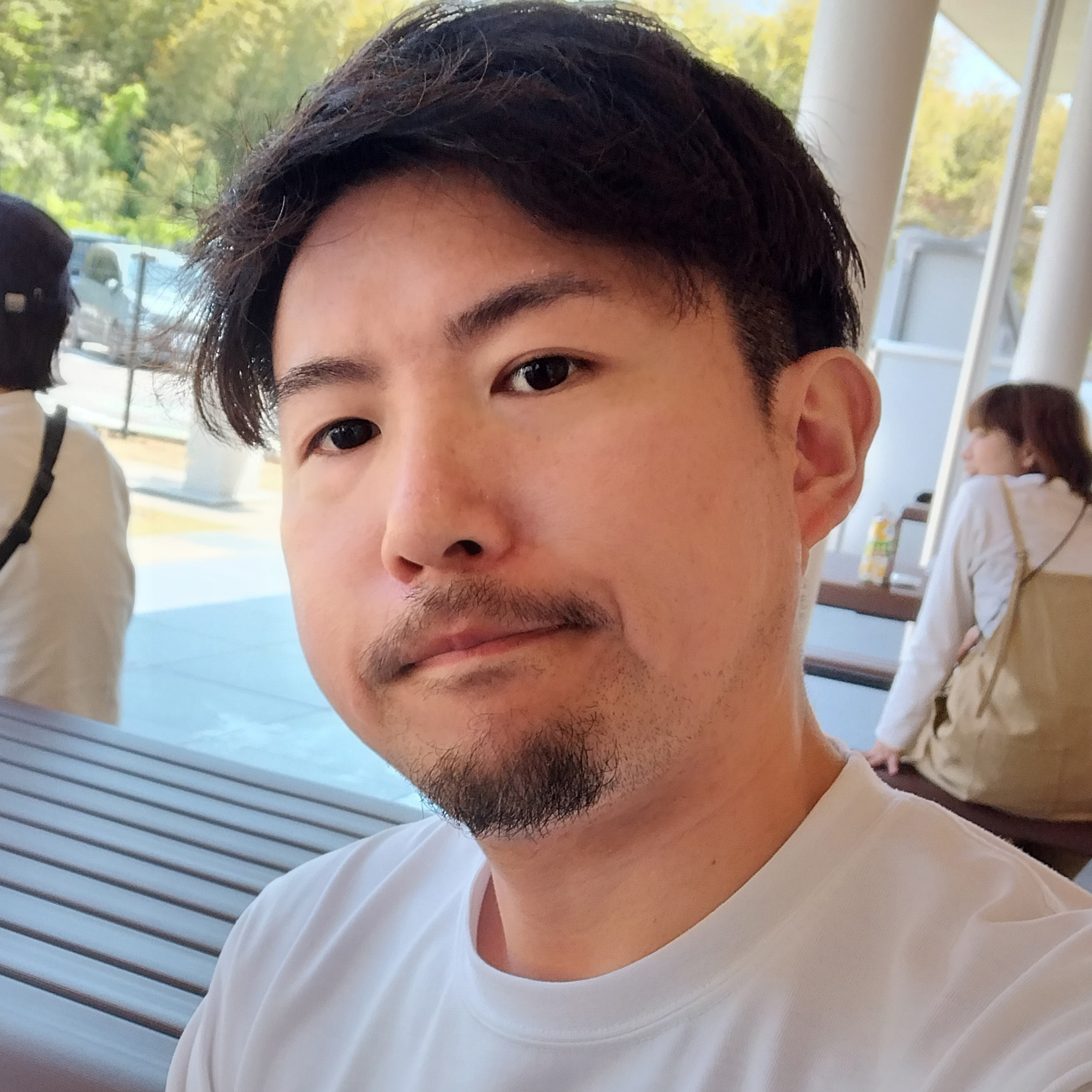 白いシャツの男性が、屋外のベンチで穏やかな表情をしています。